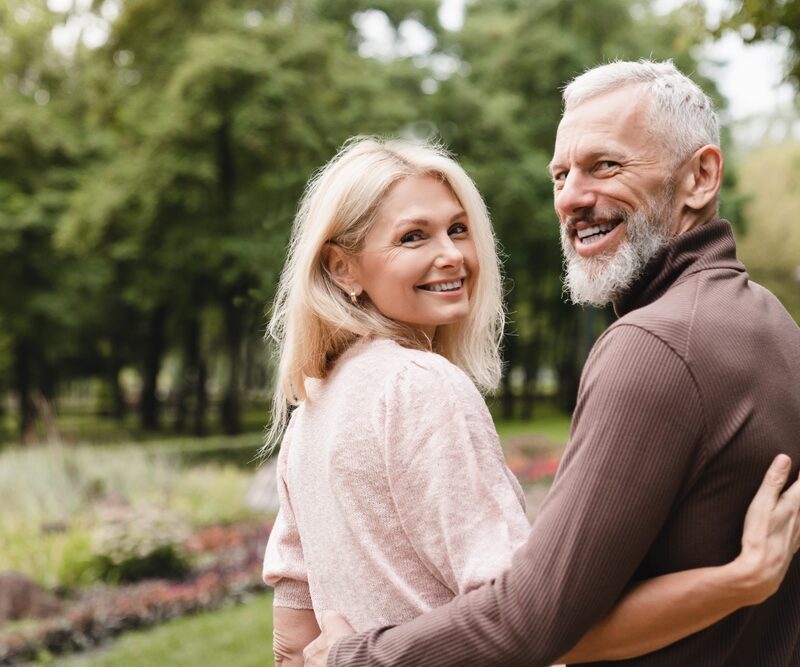 An elderly couple enjoys a walk in the park, smiling while embracing each other - migraine