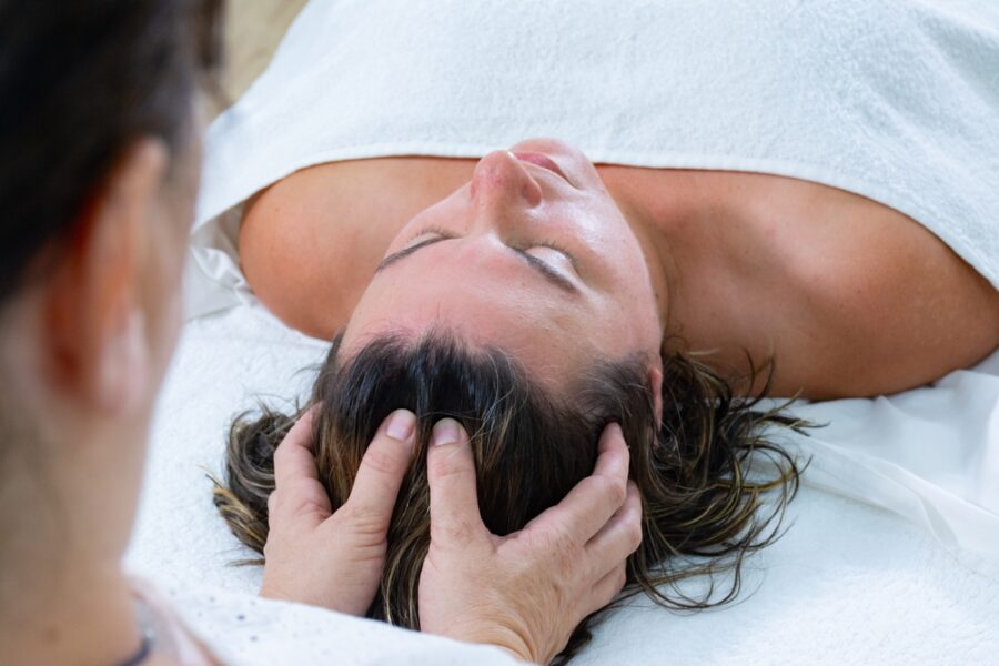 A person receives a relaxing head massage while lying on a spa bed, wrapped in a towel - Tension headache